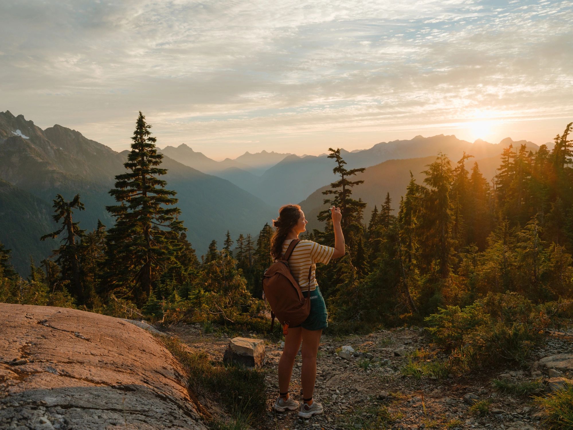Person standing on a mountain trail overlooking a wide forested landscape